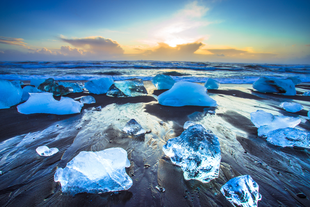 Chunks of ice on a black sand beach at sunset.