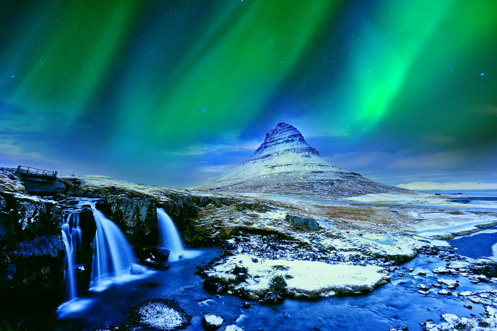 Kirkjufellsfoss Waterfall with Kirkjufell Mountain in the background and the Northern Lights overhead.