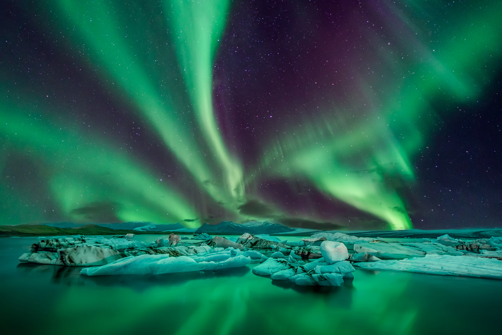 The Northern Lights in Iceland over water, snow, and distant mountains.