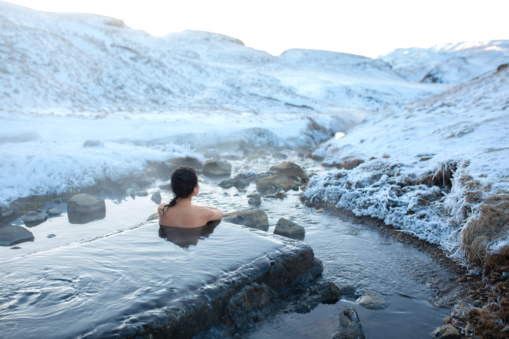 A woman sitting in Hrunalaug Hot Springs with snow all around.