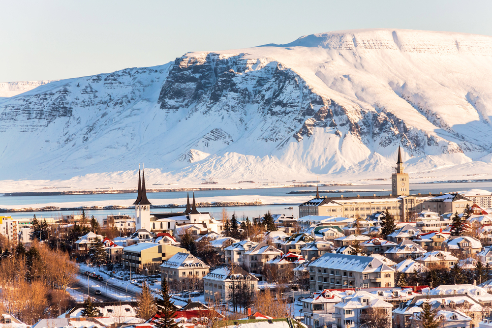 The city of Reykjavik covered in snow and golden light with a mountain in the background.