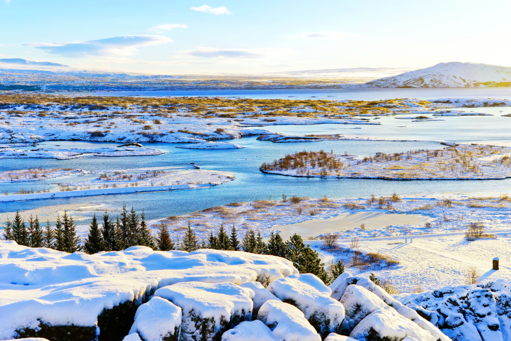 Panoramic view of Thingvellir National Park with snow, lakes, and golden hour light.