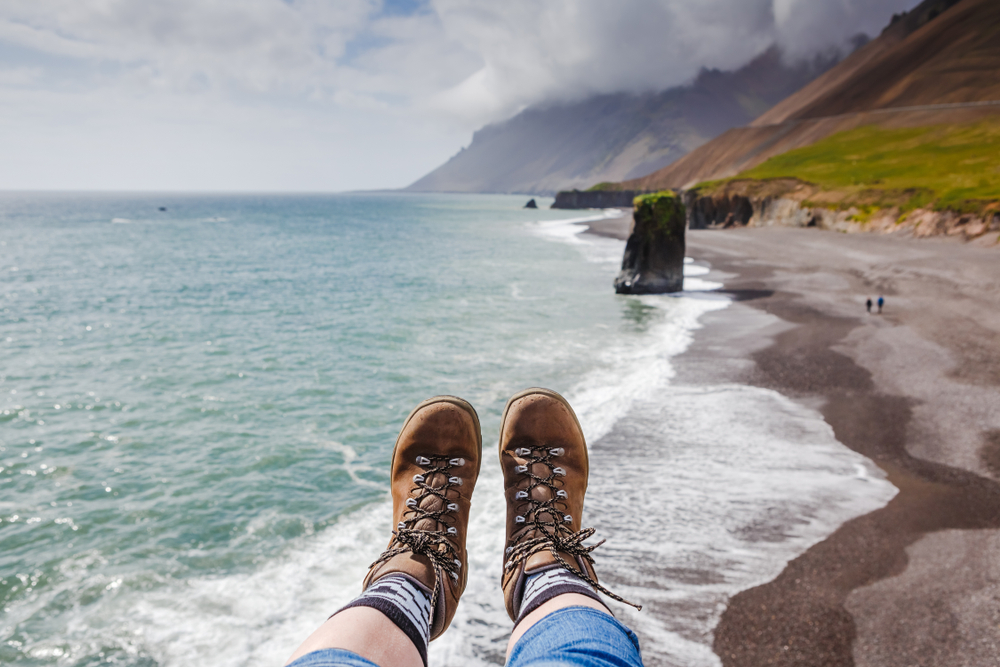 close up of woman in her hiking boots hanging her feet over a ledge with a beach below