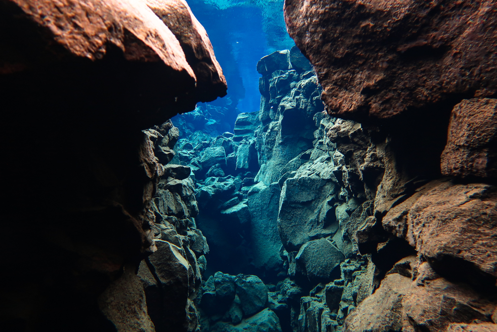 The view underwater in Silfra Fissure. It is stones on the tectonic plate and they are brown and red, but parts of the water make them look blue and green. 