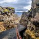 Looking down a black path between two tectonic plates that are sticking up from the Earth's crust. The trail has red guard rails and in the distance you can see people on it. One of the best things to do in Thingvellir National Park.