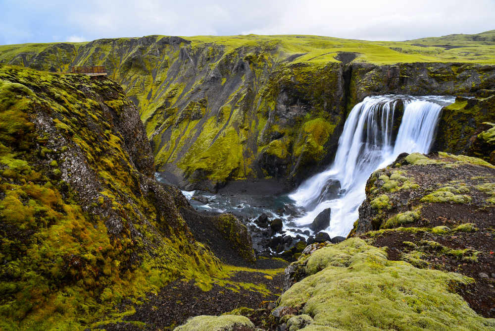 Fagrifoss waterfall nestled in green cliffs.