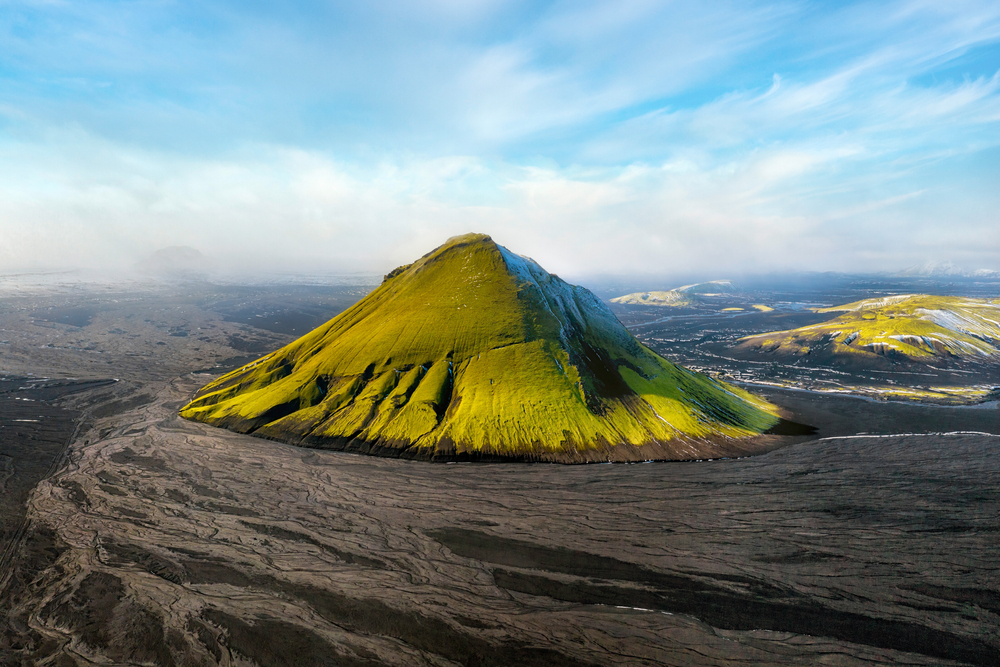 Green Maelifell sticking up in a landscape of black.