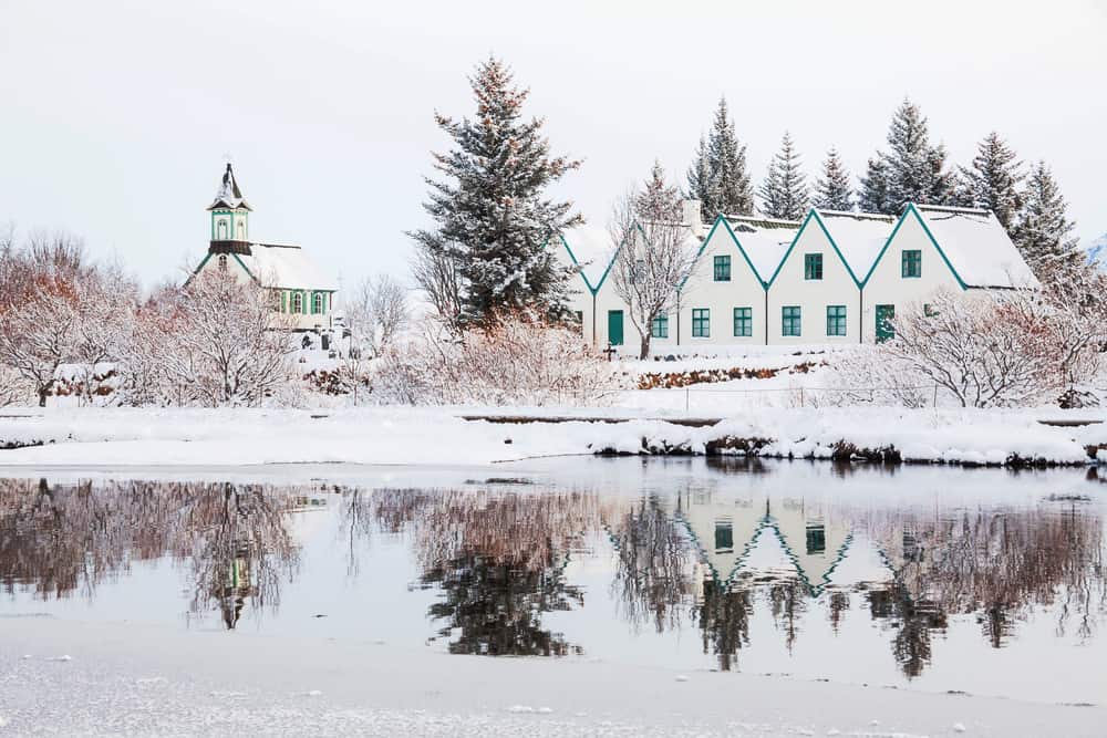 white houses with green trim and a church with the same colors covered in snow on a cloudy winter day in iceland in January 