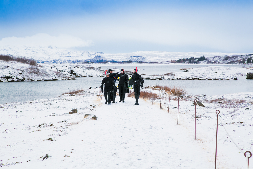 A group of dpeople walk back to their destination after their silfra snorkeling tour. There is snow on the ground around them.