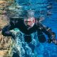 Man in a snorkel mask swims toward camera in the blue waters of the Silfra fissure