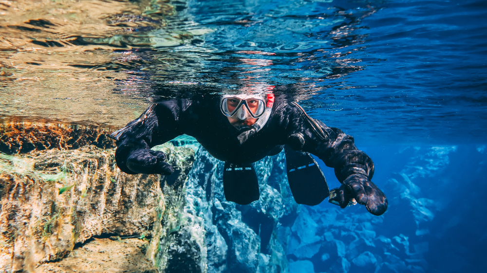 Man in a snorkel mask swims toward camera in the blue waters of the Silfra fissure