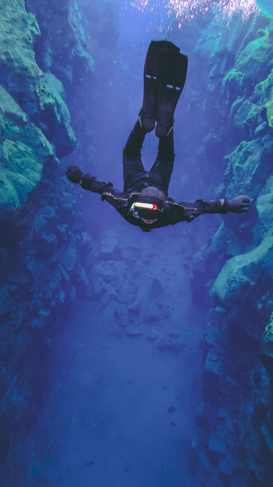 person silfra snorkeling in iceland does a backflip and floats through the blue waters, almost as if weightless.