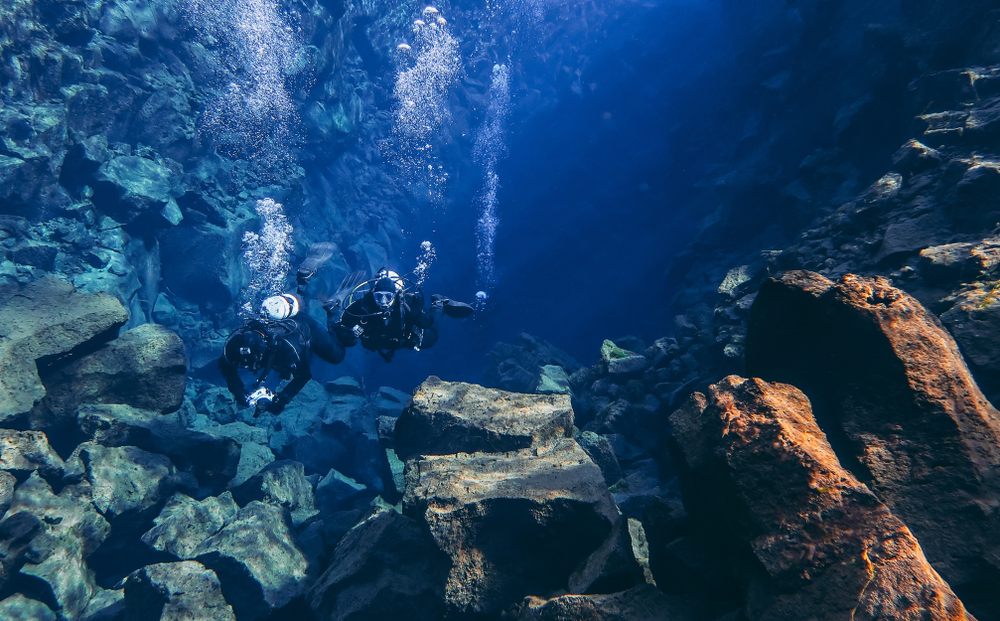 Two divers in iceland silfra fissure are deep in the fissure, their bubbles rising to the surface.