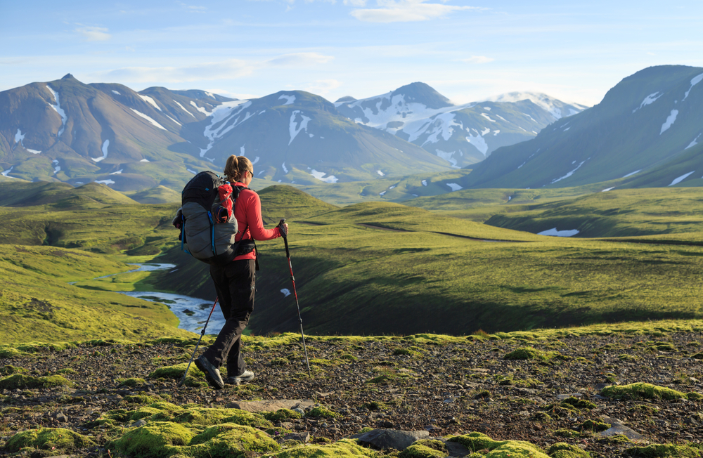 A female hiker enjoys her views of the mountains with her backpack, boots and walking sticks.