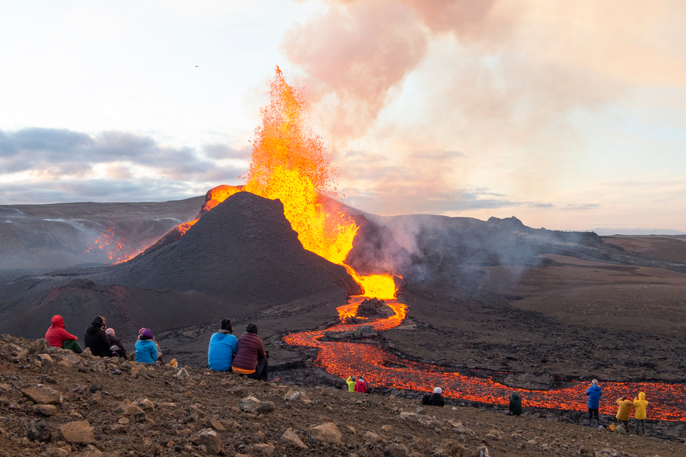 People sit and watch the eruption of lava and fire from a volcano.
