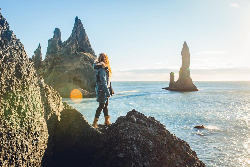 A woman overlooks the seat in Iceland while climbing on rocks
