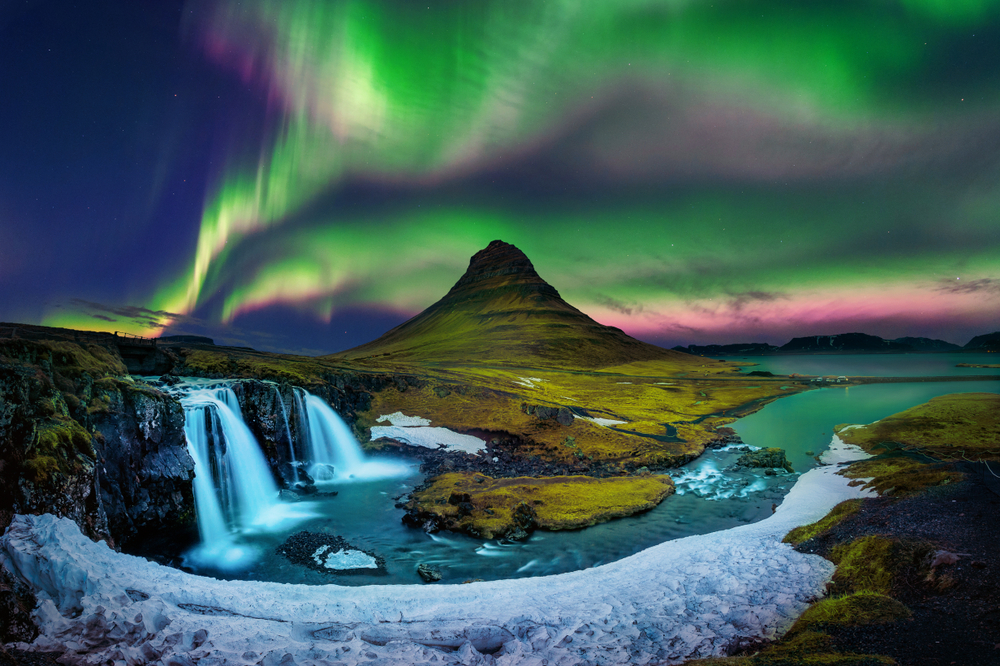 Two waterfalls and a mountain in iceland during the light show in the sky that makes it look green and purple.