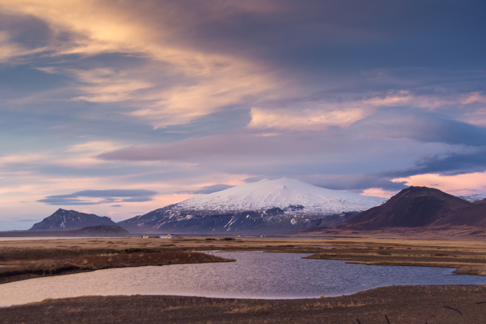 This glacier sits as a backdrop to plains in the area and is capped white with snow.