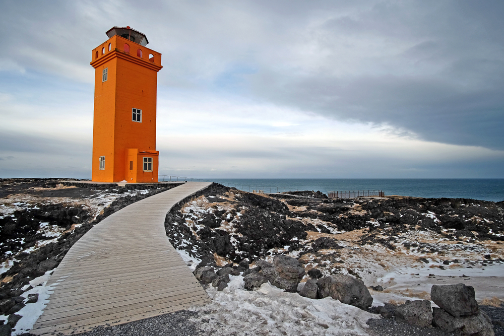 The orange color of this lighthouse contrasts the dark, black rock of Iceland.