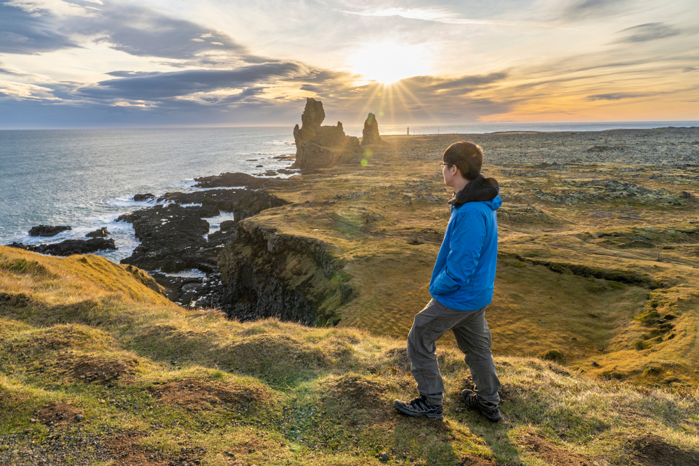 A young man looks upon a set of rock pillars during sunset in west iceland