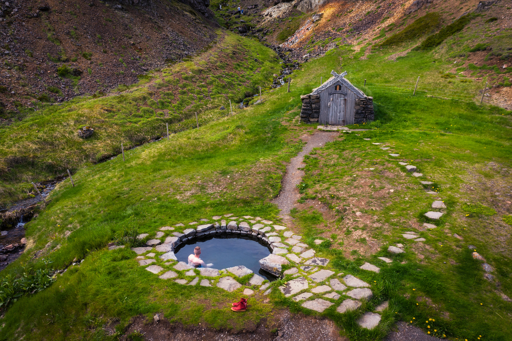 a man soaks in a tiny geothermal pool with a changing bathhouse next to him