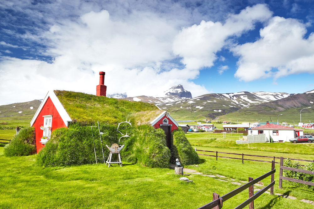 A red church sits in the front frame of the tiny town behind mountains and greenery