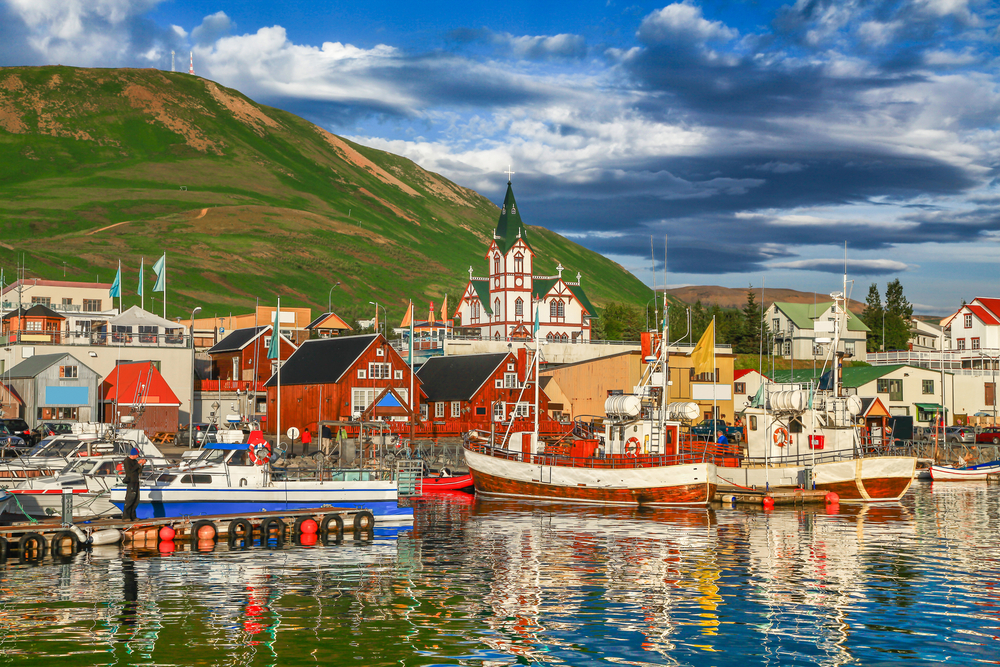 Husavik harbor with the whale watching boats docked and a green mountain in the background 