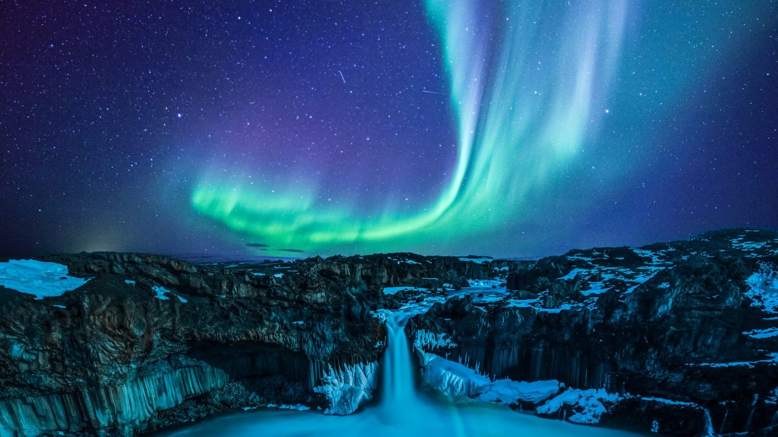 northern lights over waterfall in iceland in February