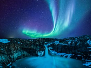 northern lights over waterfall in iceland in February