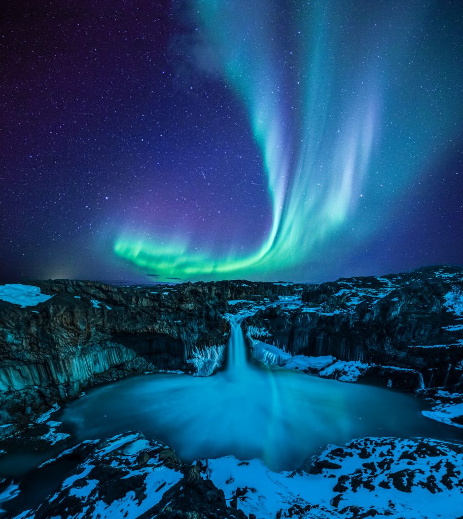 the Northern Lights dancing above a waterfall in Iceland in February
