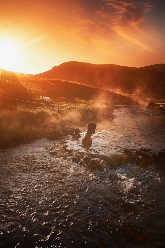 Man soaking in the Reykjadalur Hot Springs as the sun sets in Iceland in February.