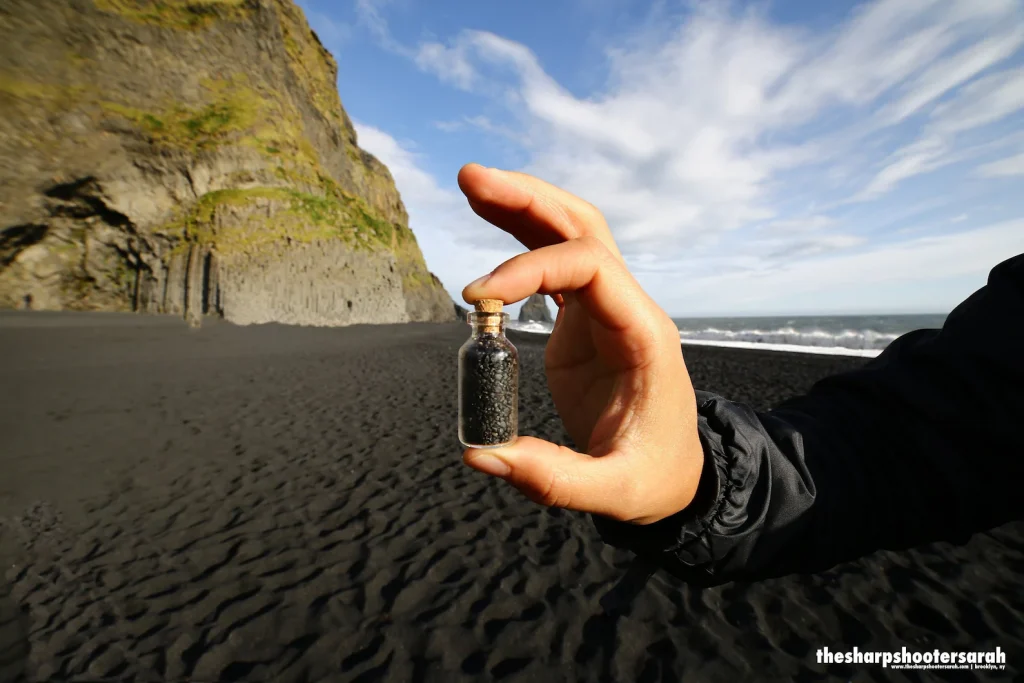 A person holding a vial of black sand.
