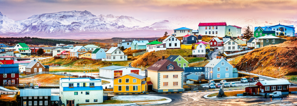 A colorful town in Iceland sits in the forefront of the photo with mountains in the back.