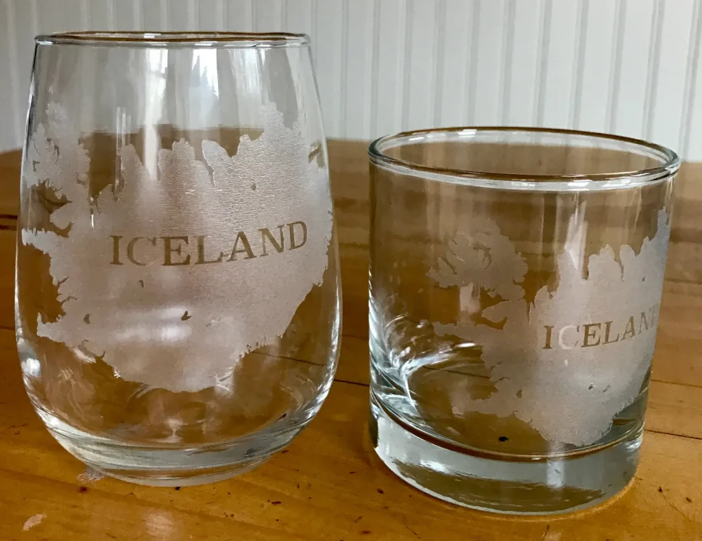 A stemless wine glass and a pint glass with an engraved map of Iceland on the front.