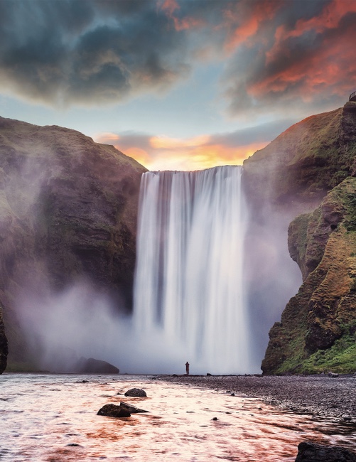 standing at the base of Skogafoss waterfall at sunset