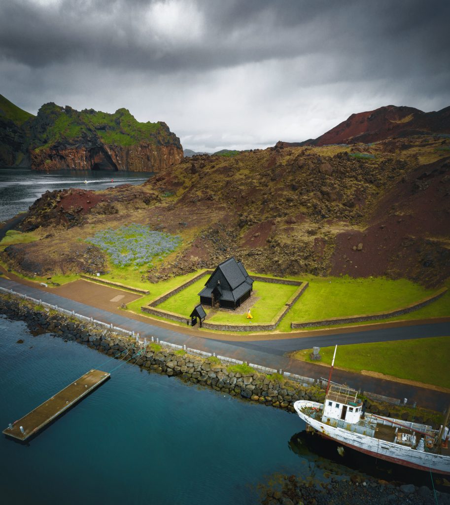 a view from above of the Heimaey stave church, the harbor, and the surrounding volcanic landscape