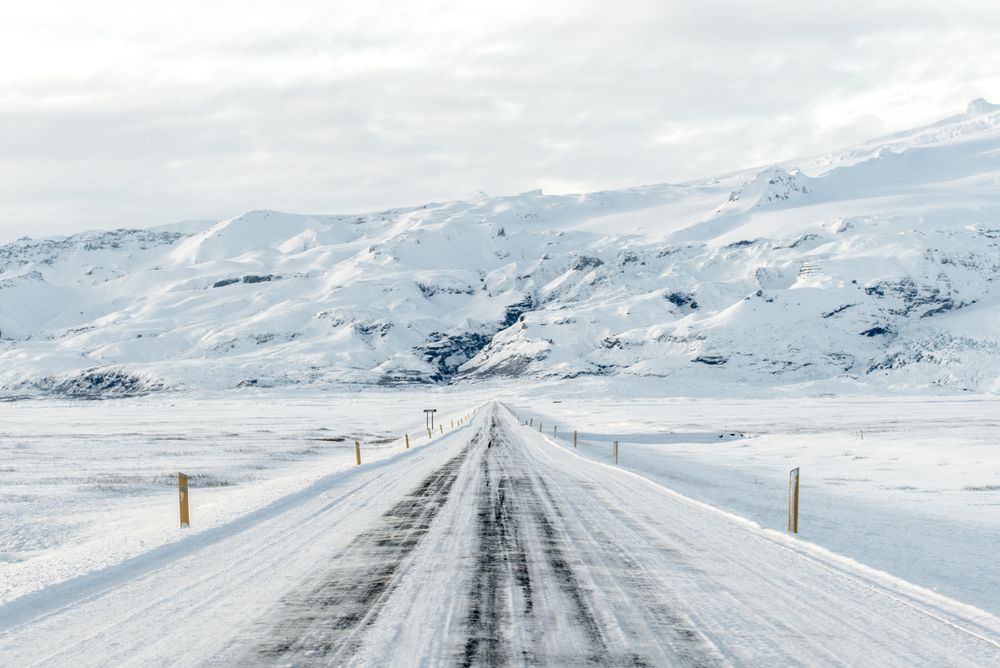 A snowy road heading straight towards mountains.