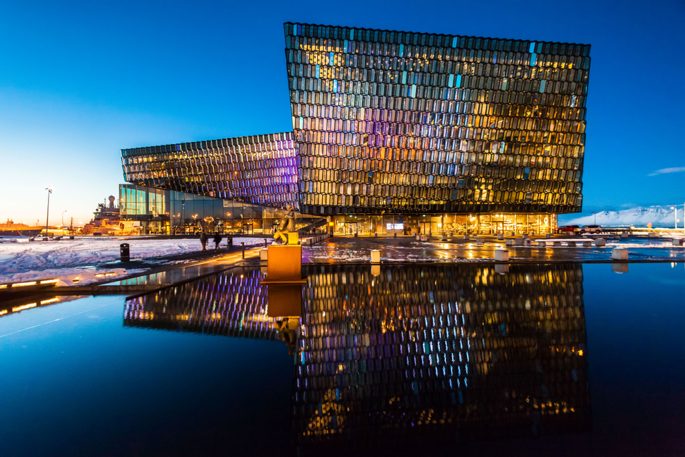 Dusk falls over the brightly colored Harpa Concert Center with a reflection in front.