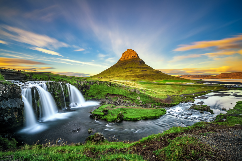 Sunset over Kirkjufell Mountain and Kirkjufellsfoss Waterfall during summer, the best time to visit Iceland for the midnight sun.