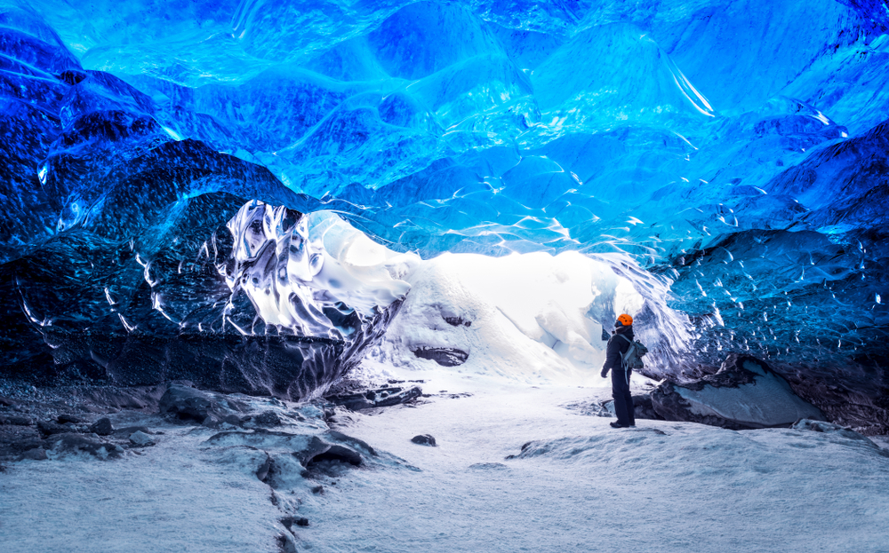 A figure standing in a blue colored ice cave in winter, the best time to visit Iceland for ice caves.