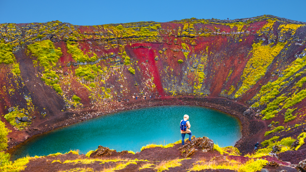 Person overlooking the blue water and colorful dirt of Kerid Crater during their tour in Iceland.