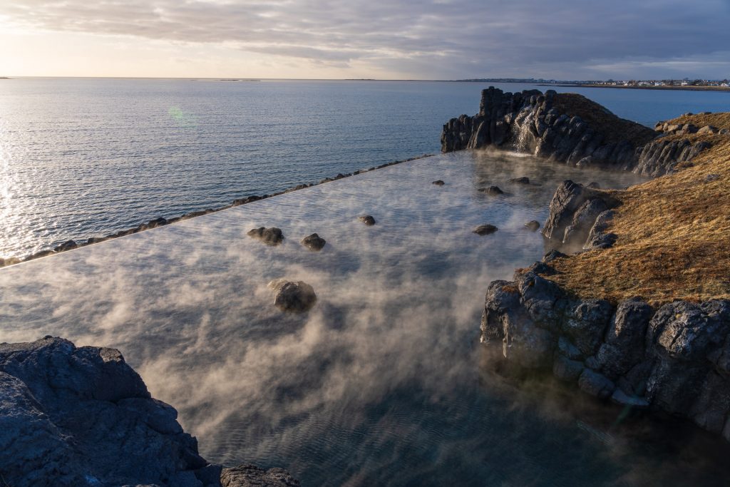 Aerial view of the steaming Sky Lagoon among cliffs and overlooking the ocean.