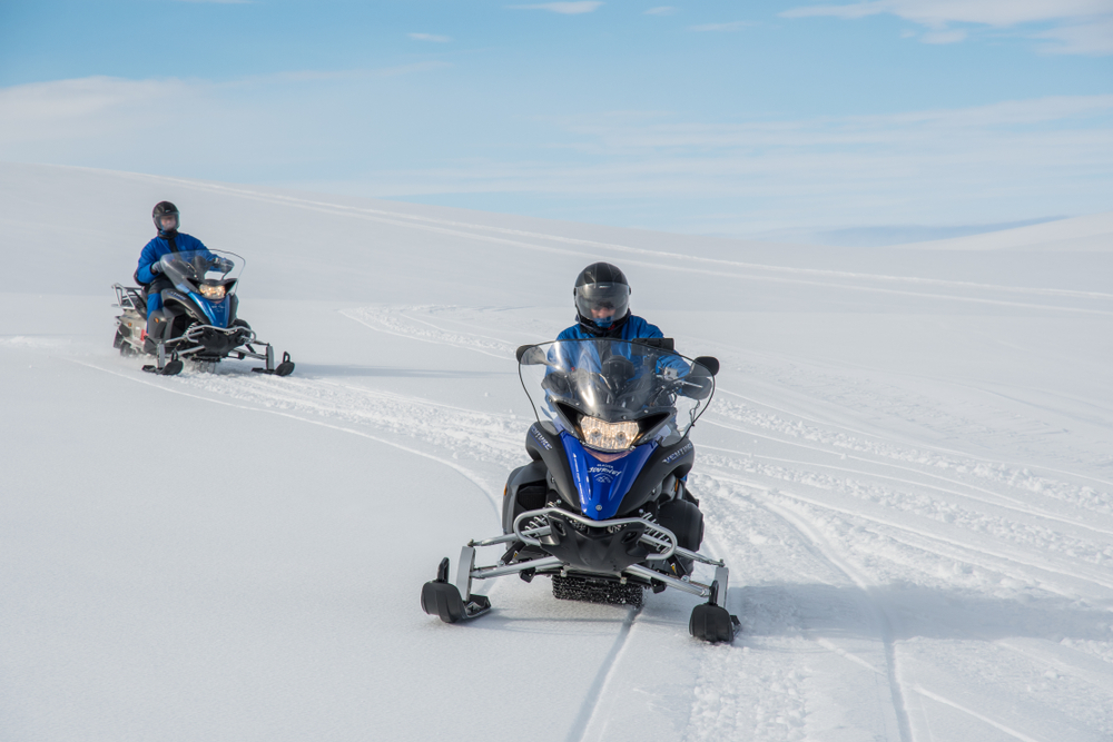 A couple of snowmobiles riding across the snow.