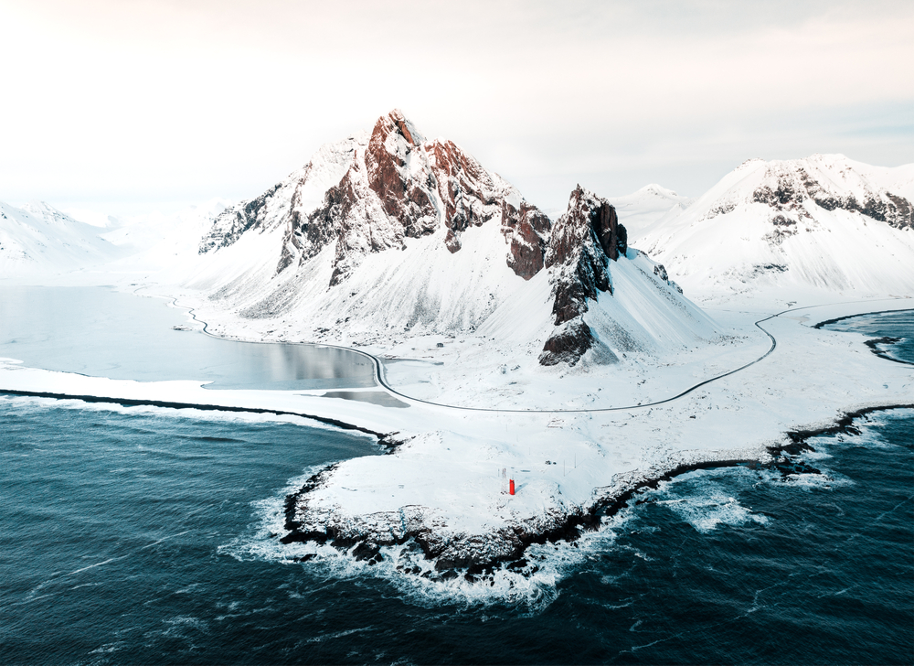 Aerial view of the shore and mountains all covered in snow.