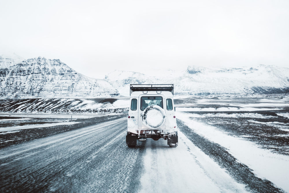 a 4x4 in Iceland driving on an icy, snow-covered road with snow covered mountains in the background