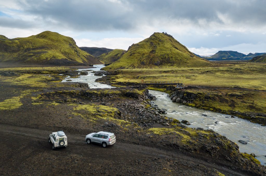 two 4wd vehicles on an f road by a river in the highlands