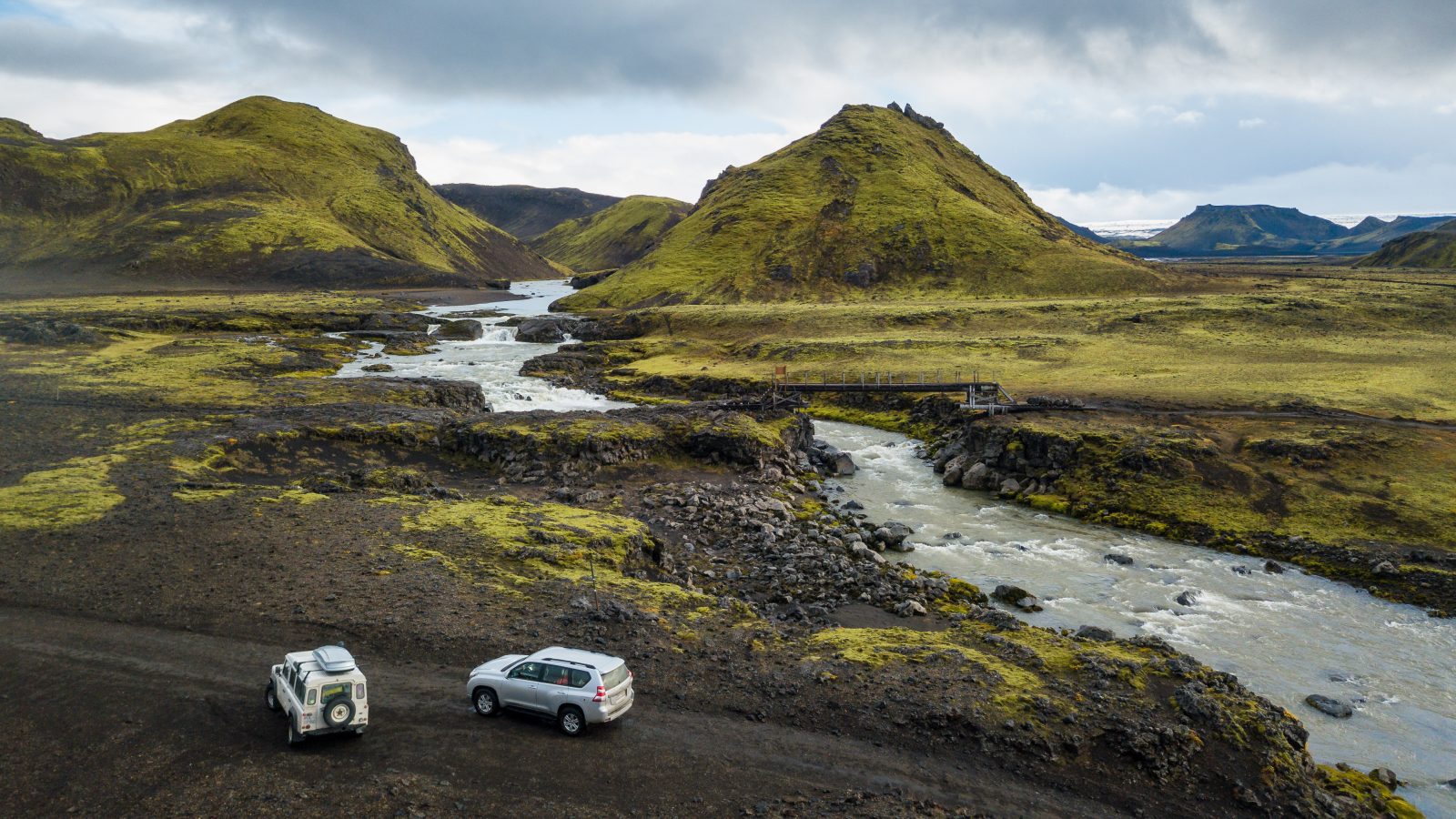 two 4wd vehicles on an F-road by a river in the highlands