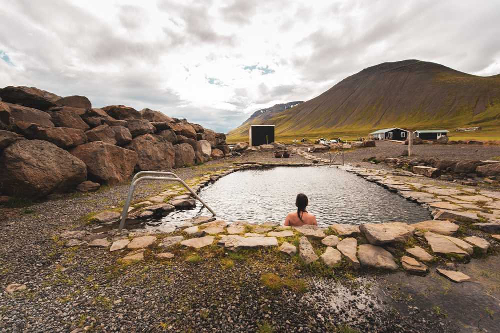Grettislaug Hot Springs surrounded by rocks with a woman sitting inside on a cloudy day.