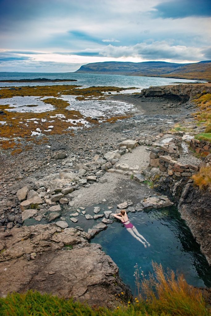 High angle view of a woman in a purple swim suit laying in a rocky hot spring in Iceland.