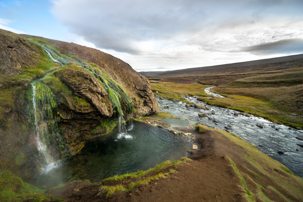 View of the Laugavallalaug Hot Spring with waterfalls flowing into a pool that connects to a river.